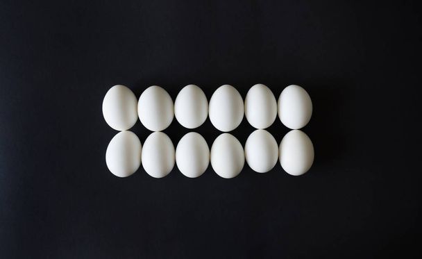 chicken eggs lie exactly in line, ordered on a black isolated background, top view - 写真・画像