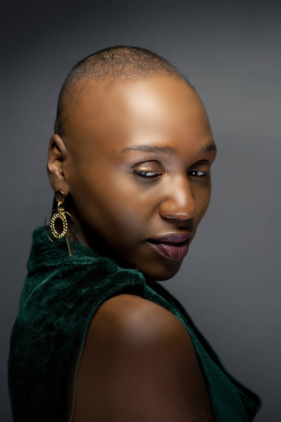 Black African American female fashion model with a bald hairstyle in a studio.  The portrait shows the beauty and confidence of the bold and trendy glamour hairdo style.   - Φωτογραφία, εικόνα