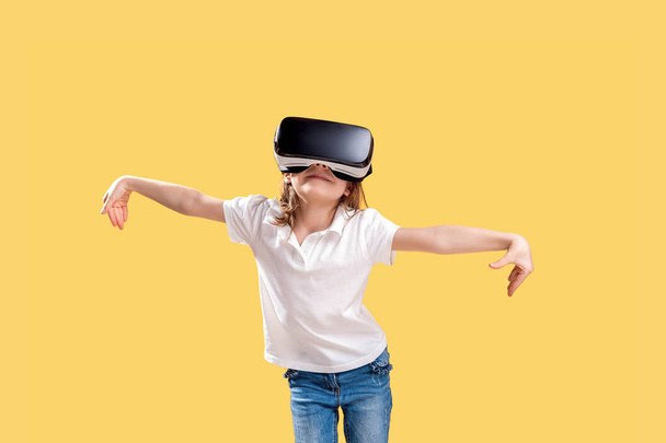 Girl 7 y.o in formal outfit wearing VR glasses putting hands out in excitement isolated on yellow background. Child using a gaming gadget for virtual reality. Virtual technology - Fotografie, Obrázek