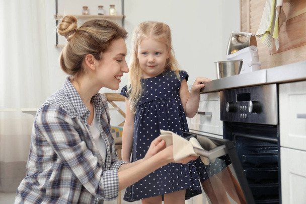 Mother and her daughter baking food in oven at home - Foto, imagen