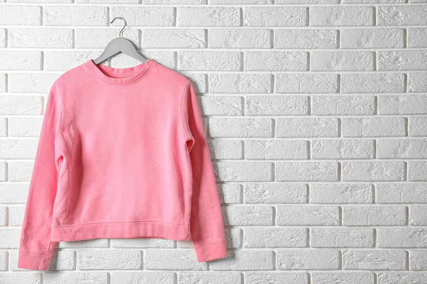 Hanger with pink sweatshirt against brick wall. Mockup for design - Fotó, kép