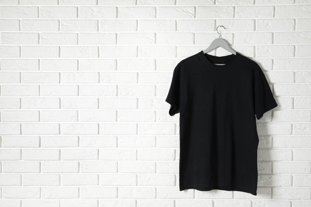 Hanger with black t-shirt against brick wall. Mockup for design - Фото, изображение