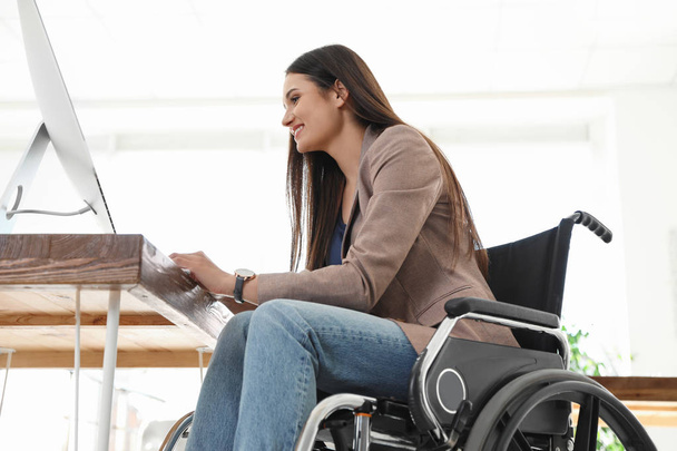 Young woman in wheelchair using computer at workplace - Foto, Bild