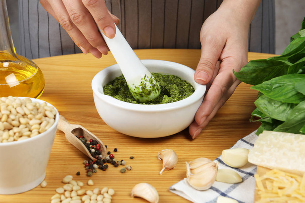 Woman mixing pesto sauce with pestle in mortar at table, closeup - Фото, изображение
