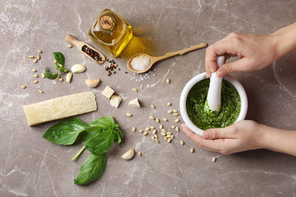 Woman mixing pesto sauce with pestle in mortar on grey table, flat lay - Fotoğraf, Görsel