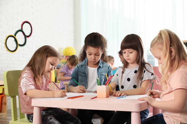Очаровательные дети рисуют вместе за столом в помещении. Развлечения в детском саду
 - Фото, изображение