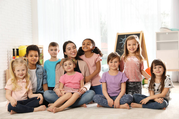 Group of cute little children with teacher sitting on floor in kindergarten - Фото, изображение