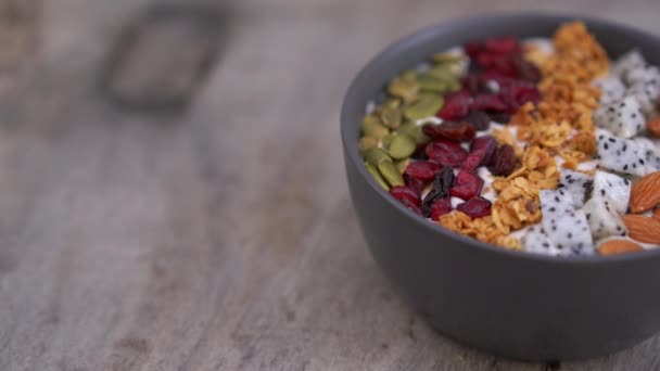 Closeup shot of a smoothie bowl with papaya, dragon fruit, granola, dried cherry, and pumpkin seeds. Healthy breakfast concept - Video, Çekim
