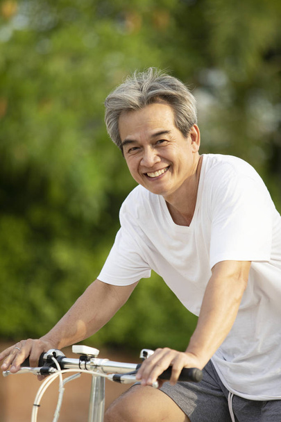 azjatycki człowiek ząb uśmiechnięty twarz jazda na rowerze w zielonym publicznym p - Zdjęcie, obraz