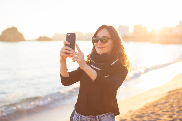 Young beautiful smiling woman making selfie on the beach enjoying sunset - Фото, зображення