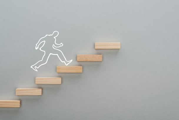 top view of drawn man running on wooden blocks symbolizing career ladder on grey background, business concept - Fotoğraf, Görsel