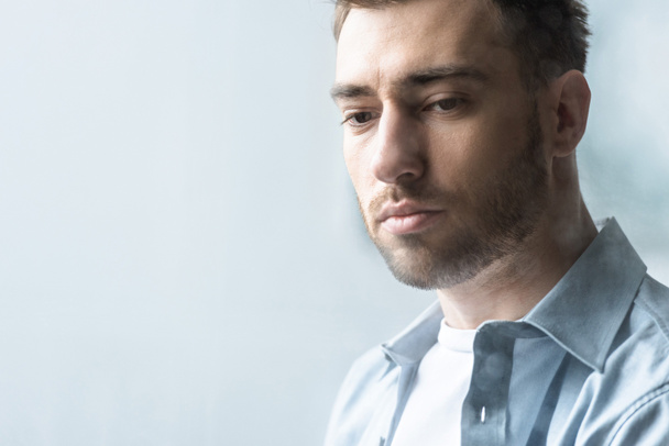 pensive bearded man in blue shirt looking down at home - Photo, Image
