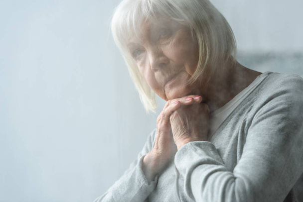 手で顔を支える灰色の髪を持つペンシブシニア女性の選択的な焦点 - 写真・画像