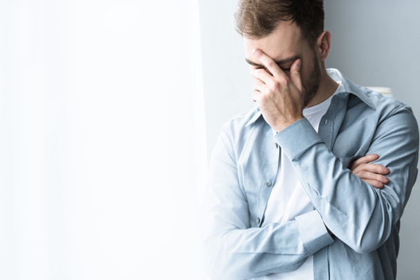 depressed man in blue shirt covering face with hand on at home - Foto, Bild