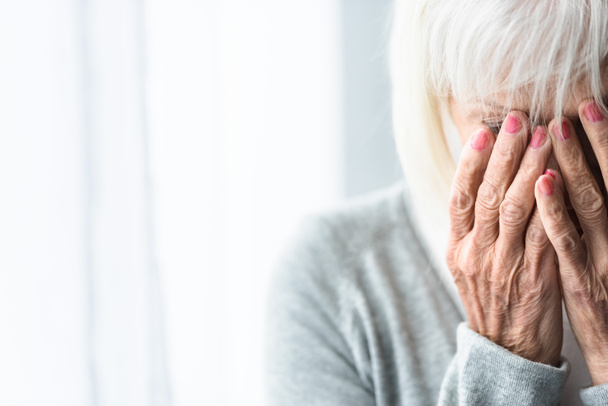 részleges kilátás sírás idősebb nő, amely arcát kézzel - Fotó, kép
