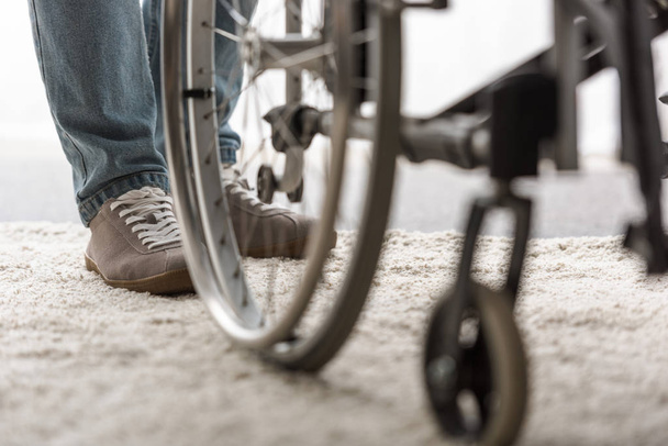 vista ritagliata di uomo in piedi su tappeto vicino sedia a rotelle
 - Foto, immagini