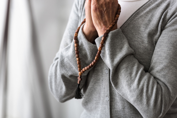 częściowy widok na starszy kobieta modląc się z drewnianym różańcem - Zdjęcie, obraz