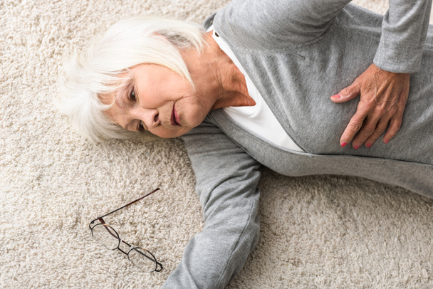 overhead view of sick senior woman lying on carpet - 写真・画像