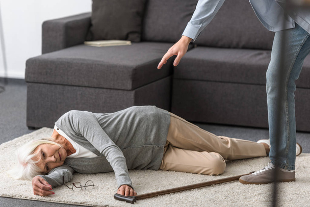 partial view of man near senior woman with walking stick lying on carpet - Foto, imagen