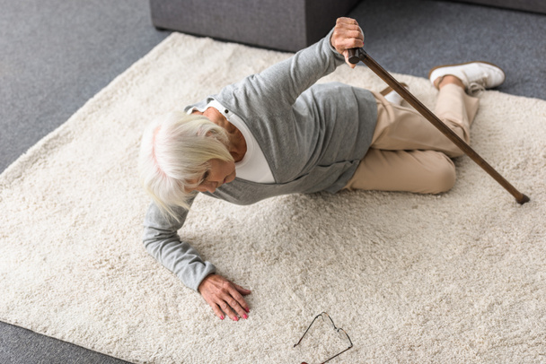 overhead view of sick senior woman with walking stick lying on carpet - Foto, Imagen