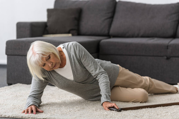 mujer anciana enferma con bastón acostado en la alfombra
 - Foto, Imagen