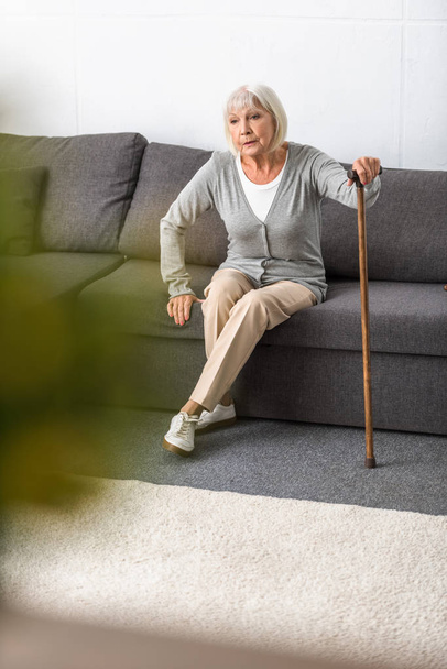 senior woman with walking stick sitting on sofa in living room - Foto, Bild