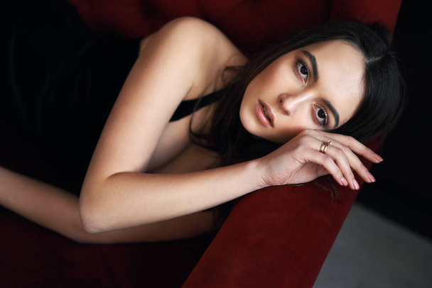 Young beautiful woman portrait posing on red sofa. Female beauty concept - Fotoğraf, Görsel