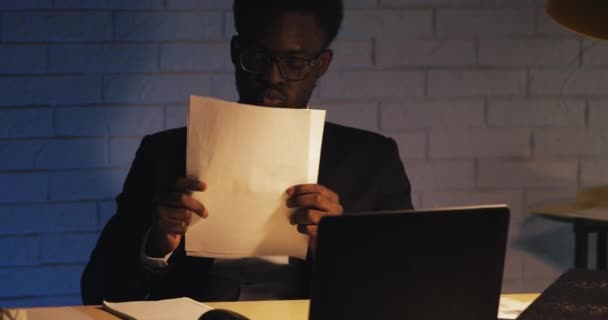Tired of working with documents young black man pushes up his glasses and rubs his eyes. Workaholic, working hard. Night time. Close up. - Záběry, video