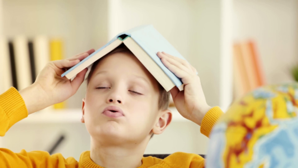 selektivní zaměření roztomilým školáku, vložení knihy do hlavy a vzdychání doma  - Záběry, video