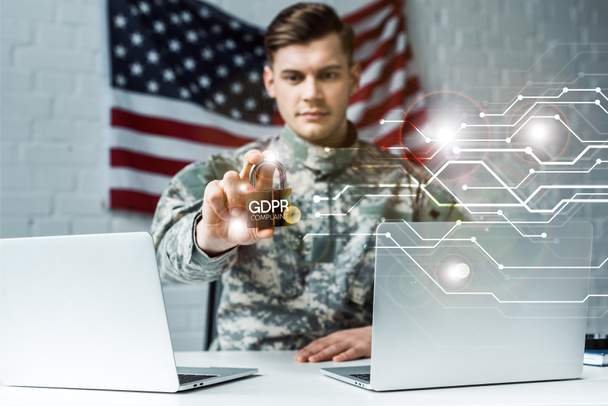 selective focus of handsome man in military uniform holding metallic padlock near laptops and gdpr lettering  - Photo, Image