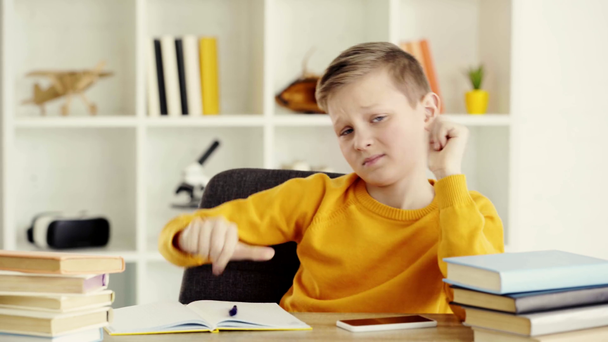 displeased kid writing in notebook near smartphone and showing thumbs down  - Video, Çekim