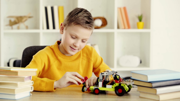 šťastný školák, který hraje s elektrickým automobilem z stavebních bloků u knih a zobrazuje palec doma - Záběry, video