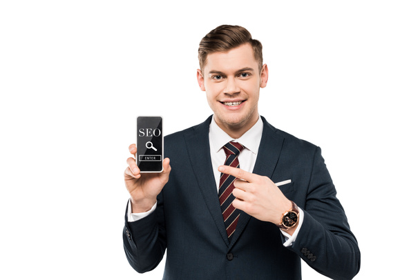 homem de negócios feliz em terno apontando com o dedo para o smartphone com seo lettering na tela isolada no branco
  - Foto, Imagem