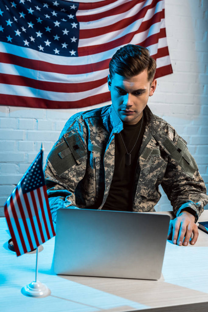 handsome soldier in uniform sitting in office and using laptop  - 写真・画像