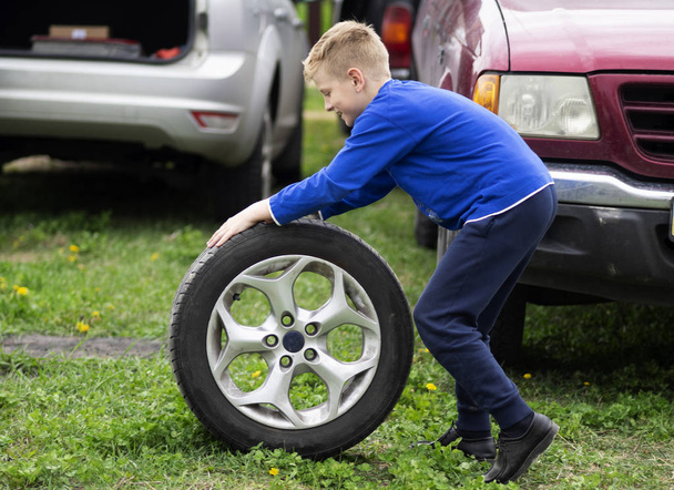 白人の少年は車の車輪を転がしている - 写真・画像