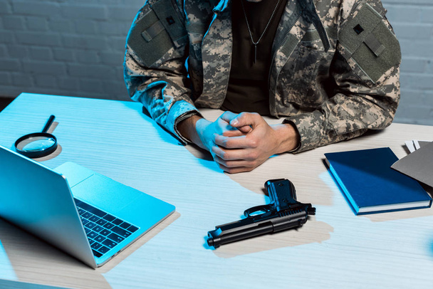 rajattu näkymä sotilas istuu puristi kädet lähellä asetta
  - Valokuva, kuva