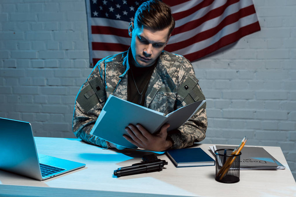 όμορφος στρατιωτικός άνθρωπος κρατώντας φάκελο, ενώ κάθονται στο σύγχρονο γραφείο  - Φωτογραφία, εικόνα