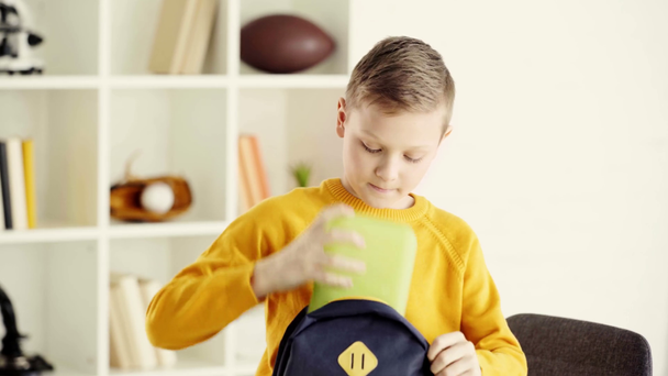 školák otvírající batoh a dávat knihy, polední box a zelený jablko  - Záběry, video