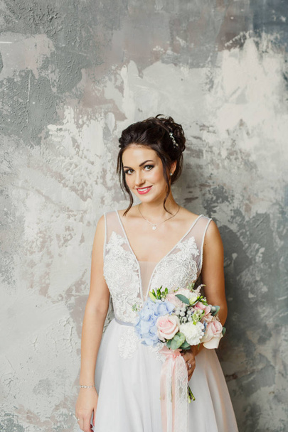 portré egy fiatal gyönyörű esküvői menyasszony egy gyönyörű elegáns ruha egy szürke háttér - Fotó, kép