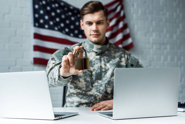 selective focus of handsome man in military uniform holding padlock near laptops - Photo, Image
