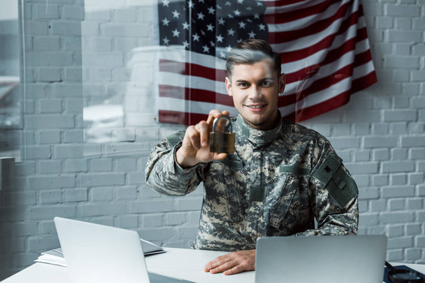 cheerful man in military uniform holding padlock near laptops - Фото, изображение