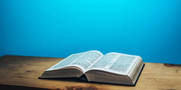 Bible on a brown wooden table. Beutiful blue wall background. - Photo, Image