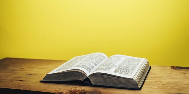 Biblia na brązowym drewnianym stole. Beutiful żółte tło ścienne. - Zdjęcie, obraz