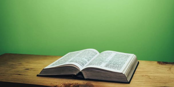 Библия на коричневом деревянном столе. Красивый зеленый фон стены
. - Фото, изображение