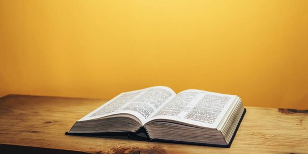 Bible on a brown wooden table. Beutiful orange wall background. - Photo, Image