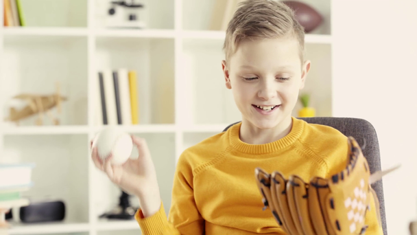 niño feliz lanzando béisbol en el aire mientras captura con guante de béisbol y sonriendo en casa
  - Metraje, vídeo