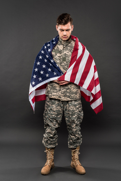 Aufgebrachter Mann in Militäruniform mit amerikanischer Flagge steht auf grau  - Foto, Bild