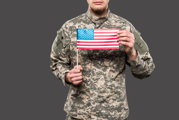 περικομμένη όψη του στρατιώτη σε ομοιόμορφη κρατώντας αμερικάνικη σημαία απομονωμένη σε γκρι  - Φωτογραφία, εικόνα