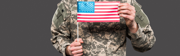 panoramatický zásah vojáka, který drží americkou vlajku izolovanou na šedé  - Fotografie, Obrázek