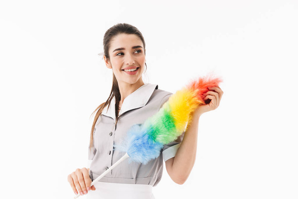 Photo of smiling maid 20s dressed in uniform holding colorful du - Foto, imagen
